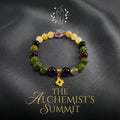 Product shot of the multi-colored Capricorn bracelet on a black background, showcasing beads in purple, yellow, black, and green. The title "THE ALCHEMIST‘S SUMMIT" is prominently displayed below in gold text.