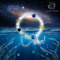 The Pisces “Oracle‘s Tide” bracelet by CosmicGlyph suspended at the mystical boundary between a starry cosmos and a deep ocean. The bracelet, with blue, yellow, and black beads and a silver fish tail pendant, glows softly amidst seaweed and stars.