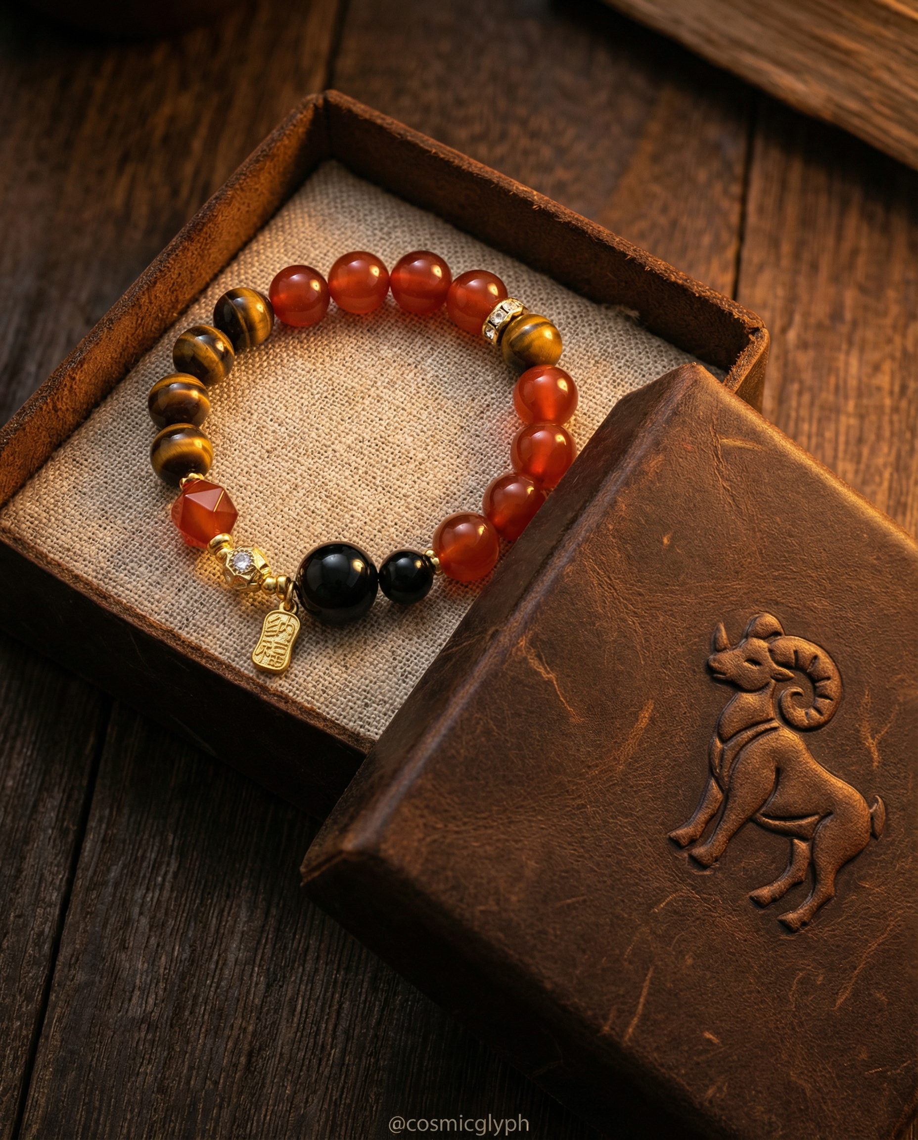 The Aries Zodiac Bracelet features beads of Red Agate, Tiger's Eye, and Black Obsidian, accompanied by a gold charm. Displayed on a rich wooden table for an elegant, warm presentation.